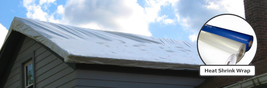 Clear heat shrink wrap covering a gable roof on a gray-sided house as a temporary weather barrier until repairs